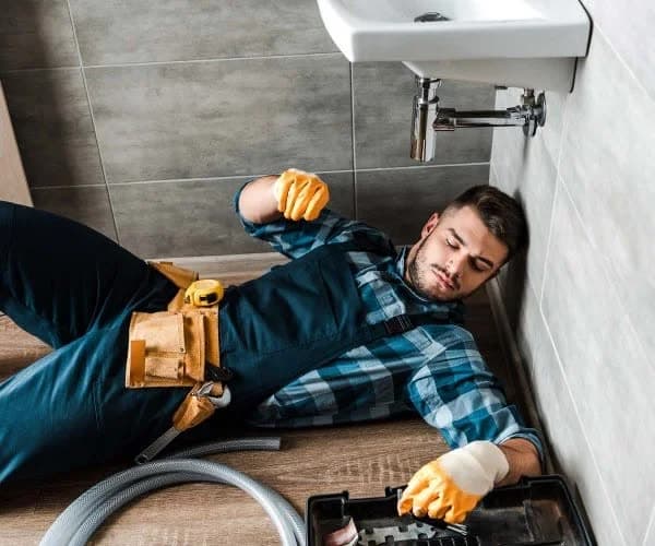 Handyman working at floor level beside a bath with a toolbox